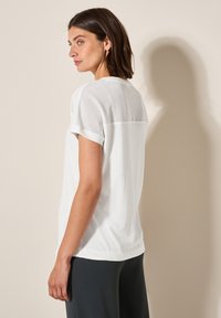 T-shirt blanc à manches courtes, avec un panneau en mesh sur le haut du dos. Tissu en coton doux avec une coupe décontractée et un ourlet arrondi.