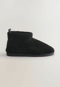 Papuci negri, texturat, cu un material exterior moale și pufoasă. Design la înălțimea gleznei, cu vârf rotund și o talpă plată, flexibilă.