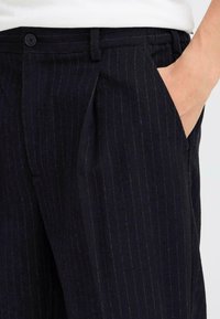 Marineblauwe broek met streepjes, gemaakt van gestructureerde stof, voorzien van een zijzak, knoopsluiting en tailleurplooien aan de voorkant voor een gestructureerde pasvorm.