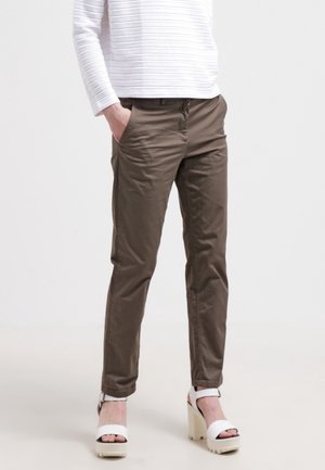 Person iført olivengrønne slim-fit bukser, hvid langærmet top og hvide platformsandaler med høj hæl og åbne tæer.