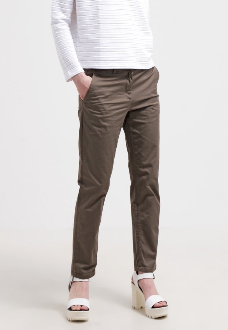 Osoba ubrana w oliwkowozielone wąskie spodnie, biały długi rękaw oraz białe sandały na platformie na wysokim obcasie z odkrytymi palcami.