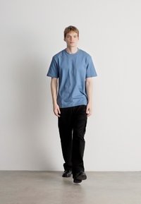 Μπλε βαμβακερό μπλουζάκι με κοντά μανίκια και στρογγυλή λαιμόκοψη. Συνδυάζεται με μαύρο, άνετο cargo παντελόνι και μαύρα παπούτσια.