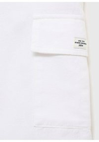 Bijela tkanina zakrpa s preklopom, s oznakom "MNG TEEN GENUINE GARMENTS 1984." Ujednačena tekstura i čiste šavove.