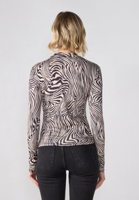 Haut à manches longues en tissu extensible avec un imprimé zèbre abstrait beige et marron foncé. Design cintré avec un col rond.