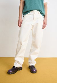 Pantaloni bianchi a gamba larga in cotone, con vita alta, chiusura anteriore con bottone e due tasche laterali, abbinati a scarpe con accenti viola.