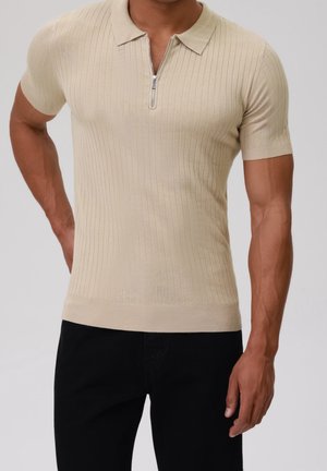 Beige kortärmad polo skjorta med dragkedja framtill, strukturerad ribbad design och en åtsittande silhuett, tillverkad av ett mjukt, stretchigt material.