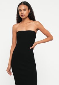 Μαύρο ριγωτό strapless φόρεμα με κομψή σιλουέτα, ομαλή υφή και ευθείες λαιμόκοψη, σχεδιασμένο για μια κομψή και μινιμαλιστική εμφάνιση.