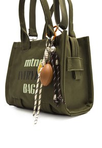 Olivgrüne Canvas-Tasche mit doppelten Griffen, Reißverschlussverschluss und dekorativen Schlüsselanhängern, darunter ein kleiner Fußball und Schnüre.