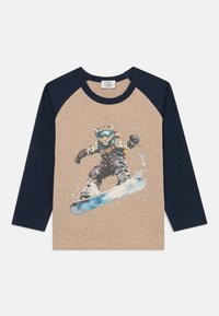Majica s dugim rukavima bež boje s tamnoplavim rukavima. Ima grafiku snowboardera u akciji, s plavim snowboardom.