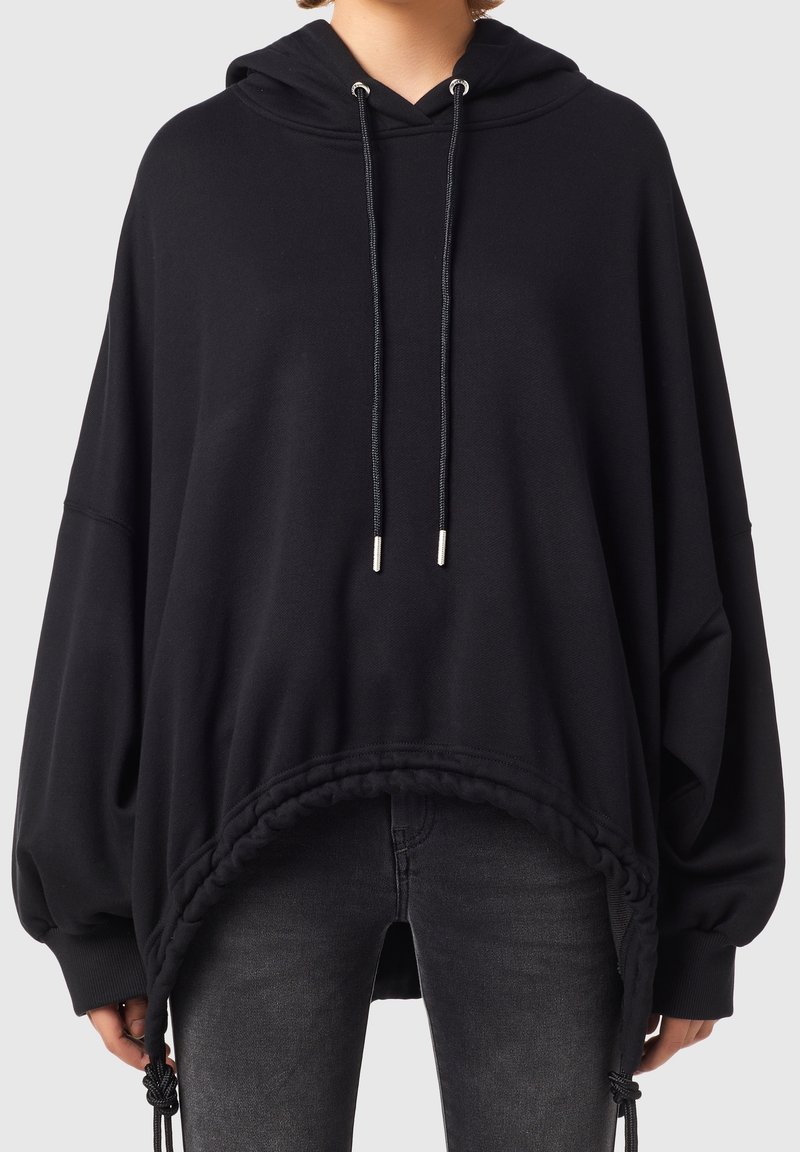 Svart oversized hoodie med dragsko i huvan, elastisk nederkant och flätad accent. Tillverkad av mjukt tyg med en slät yta.
