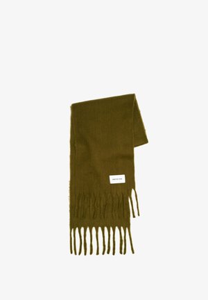 Olivengroene sjaal van zachte wol met franjes aan de randen, met het label "ARCTIC FOX", gedragen over een wit t-shirt met zwarte geplooide broek.