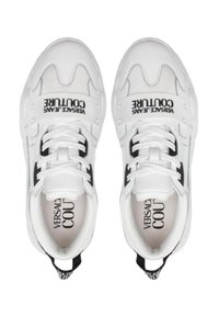 Baskets blanches avec un tissu texturé, des accents noirs et des lacets. Présente un logo sur les côtés et une boucle à l'arrière pour un enfilage facile.