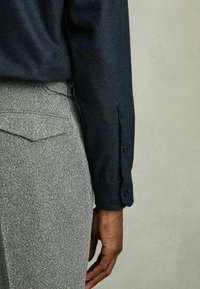 Marineblauwe button-up blouse met een gestructureerde afwerking, gecombineerd met grijze geblokte broeken met een achterzak en riemlussen.
