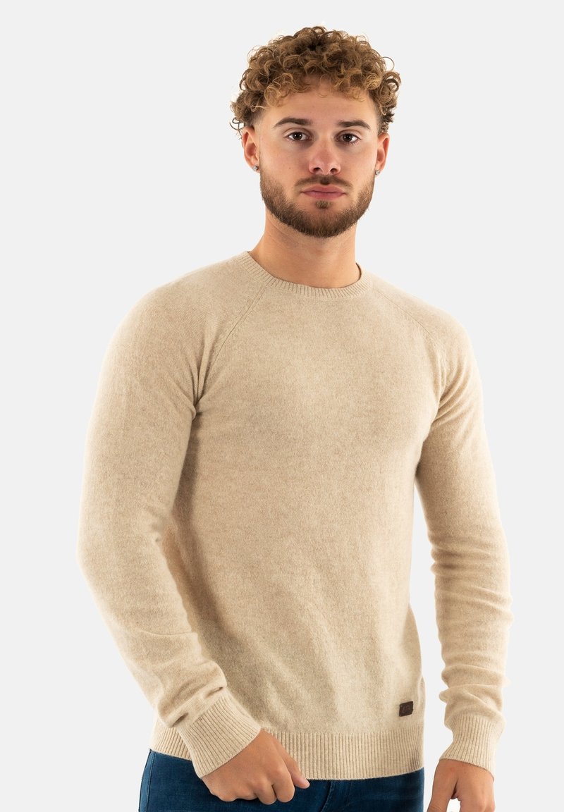 Maglione in lana beige con maniche lunghe, scollatura rotonda, polsini e orlo a coste. Presenta una piccola etichetta con logo in basso a sinistra.