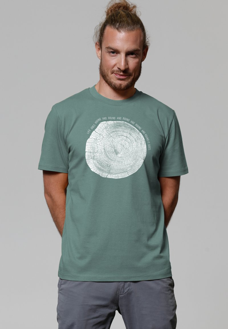Grünes Baumwoll-T-Shirt mit einem weißen runden Grafikdesign, das einem Baumring ähnelt, mit Text um das Muster herum. Kurze Ärmel und Rundhalsausschnitt.
