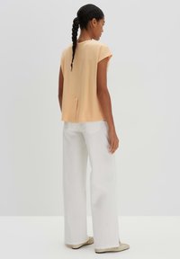 Perzikkleurige blouse met korte mouwen en een plooi aan de achterkant, gecombineerd met wijde witte broek en beige flats. Glad textuur, minimalistisch ontwerp.