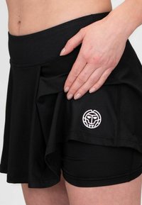 Falda corta atlética negra con una cinturilla texturizada, diseño en capas y un logo circular en blanco en el costado, con un forro corto interior.