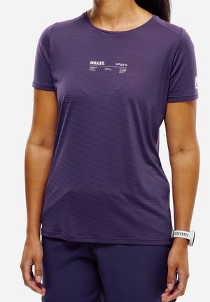 Femme portant un maillot de sport violet ajusté à manches courtes et un short assorti, avec une montre blanche au poignet gauche.