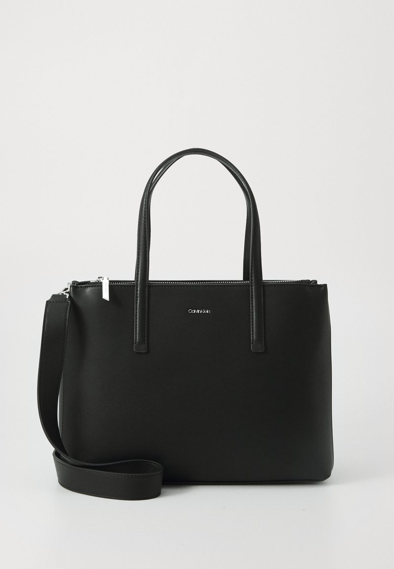 Borsa a tracolla nera realizzata in materiale liscio con due manici corti e una tracolla rimovibile. Presenta una chiusura superiore con zip e un dettaglio del logo frontale.