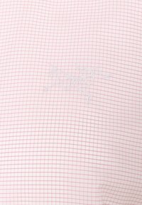 Tissu blanc avec un motif à carreaux rose et un logo discret brodé d'un lézard stylisé en fil blanc.