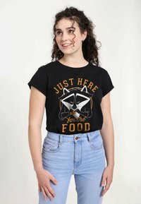 Sort t-shirt med korte ærmer, der viser en grafik af en vaskebjørn og teksten "BARE HER for MADEN" i orange og hvid. Bæres med lyseblå jeans.