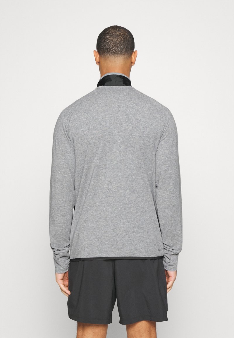 Camiseta deportiva gris de manga larga con cuello negro, que presenta un ajuste relajado y una textura suave, combinada con pantalones cortos negros.