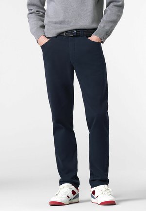 Marineblaue Chinos aus glattem Stoff, mit seitlichen Taschen, schmaler Passform und kombiniert mit weißen Sneakers mit roten Akzenten.