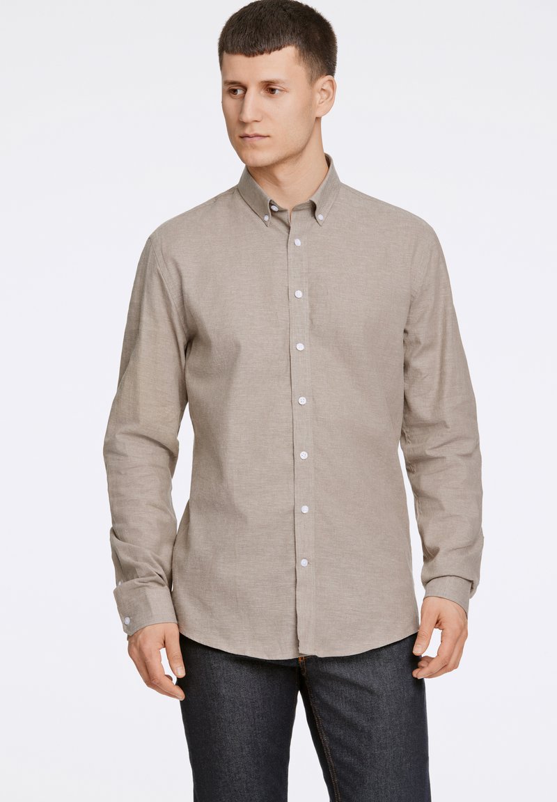 Lichtbruine button-up shirt met lange mouwen, gestructureerde kraag, witte knopen en een zachte, gestructureerde stof. Gemaakt in combinatie met donkere jeans.