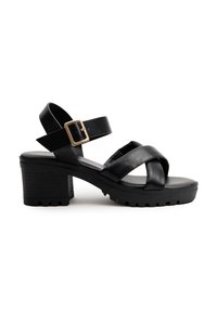 Sandalias de tacón negro con suela gruesa, con correas cruzadas y una hebilla ajustable. Fabricadas en cuero suave con un tacón texturizado.