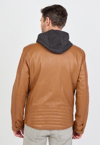 Brun læderjakke med en grå hætte. Har en glat tekstur, tætsiddende design og quiltede detaljer langs den bageste kant og ærmerne.