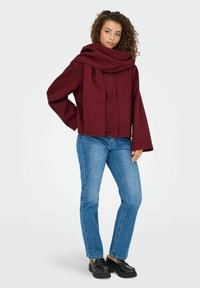 Bordeaux uldblandede frakke med brede ærmer og en draperet tørklædekrave, parret med blå jeans og sorte platform sko.