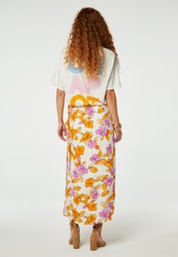 Rijgrok in het wit met paarse en oranje bloemen. Heeft een lichtgewicht stof, een zijsstrik en een vloeiende uitstraling. Bruine sandalen met blokhak.
