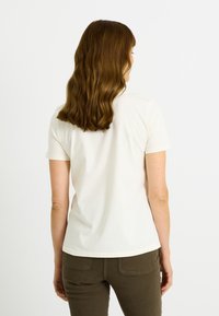 Camiseta blanca de manga corta hecha de tejido suave, con cuello redondo y forma ligeramente ajustada, combinada con pantalones verde oliva.