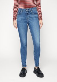 Jeans de tiro alto de color azul con un ajuste slim, fabricados en denim. Presentan un diseño clásico de cinco bolsillos y un ligero desgaste a lo largo de los muslos.