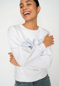 Sudadera blanca con estampado floral en tonos azules, cuello redondo y puños acanalados. Tejido suave y corte relajado.