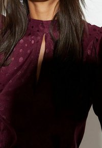 Blusa bordeaux con un delicato motivo a pois, caratterizzata da un collo a chiave e un tessuto fluido. Morbida al tatto e dalla vestibilità comoda.