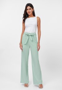 Light green wide-leg trousers with bow tie at waist paired with a white sleeveless top. Smooth fabric with a tailored fit. Minimalist design.