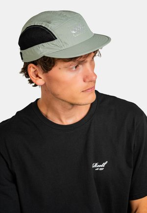 Light green cap with a flat brim, featuring black mesh panels on the sides and a logo patch at the front. Worn with a black T-shirt.