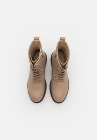 Bottines en cuir tan avec un laçage et une fermeture éclair sur le côté, bout rond, dessus texturé et semelle en caoutchouc noire. Talons plats et languettes de traction.