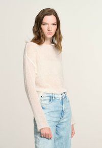 Maglione leggero e trasparente in un morbido colore chiaro, con maniche lunghe e una vestibilità rilassata, abbinato a jeans in denim blu chiaro a vita alta.