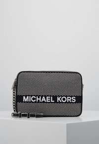 Black and white striped rectangular bag with a silver chain strap and “MICHAEL KORS” logo on a solid black panel. Textured surface details.