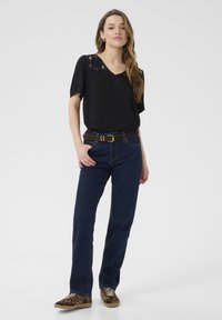 Blouse noire à manches courtes avec des détails en dentelle aux épaules, associée à un jean droit bleu foncé et une ceinture marron, complétée par des baskets imprimées léopard.