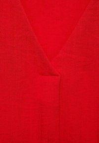 Tessuto rosso con un design a scollatura a V e una superficie leggermente testurizzata. Una piccola tasca è visibile sul frontale, che ne aumenta la funzionalità.