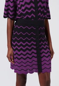Abito lavorato a maglia a ondulazioni viola e nero con maniche corte, vita a costine, bottoni davanti e orlo a scallop.