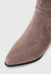Taupe suede ankle boot with a pointed toe, smooth texture, side stitching detail, and a black rubber outsole.