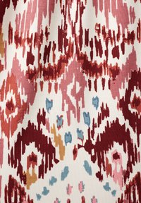 Textiel met een abstract patroon met tinten rood, roze en blauw op een witte achtergrond, met een textuurachtig stofontwerp.