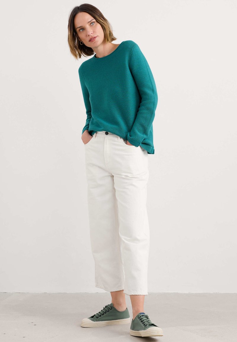Tegelse ribbeltrui, witte brede jeans, groene sneakers met beige zolen. Casual stadsoutfit met een relaxte pasvorm en strakke lijnen.