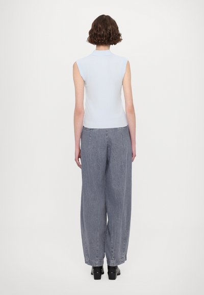 Lichtblauwe mouwloze gebreide top met een kraag, gecombineerd met hoog-taille grijze jeans met een wijde pijp en een gestructureerde afwerking. Zwarte schoenen.