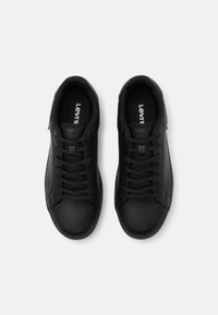 Sorte lær sneakers med snøredesign, som har en strukturert overflate og et lite rødt accent. Merkenavn trykket på innsiden av sålen.