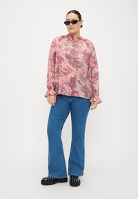 Blusa floreale rosa con maniche a volant, abbinata a jeans a zampa blu e scarpe con plateau nere. Gli occhiali da sole completano l'outfit.